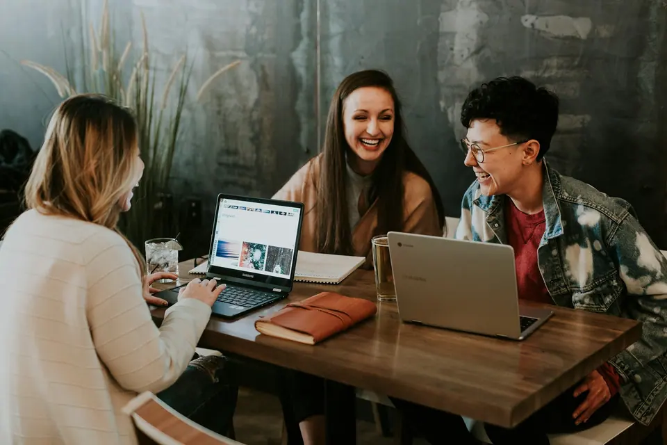 Três pessoas sorrindo em volta de uma mesa com notebooks e cadernos abertos